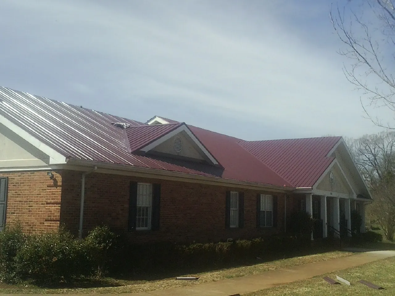 Red metal roof with gabled entries on a long brick building, from a Hail Damage Roof Repair job in Umatilla
